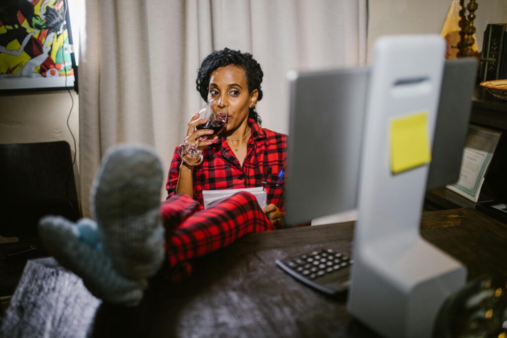 Home Woman in red pajamas relaxing with wine at a home office desk with feet up.